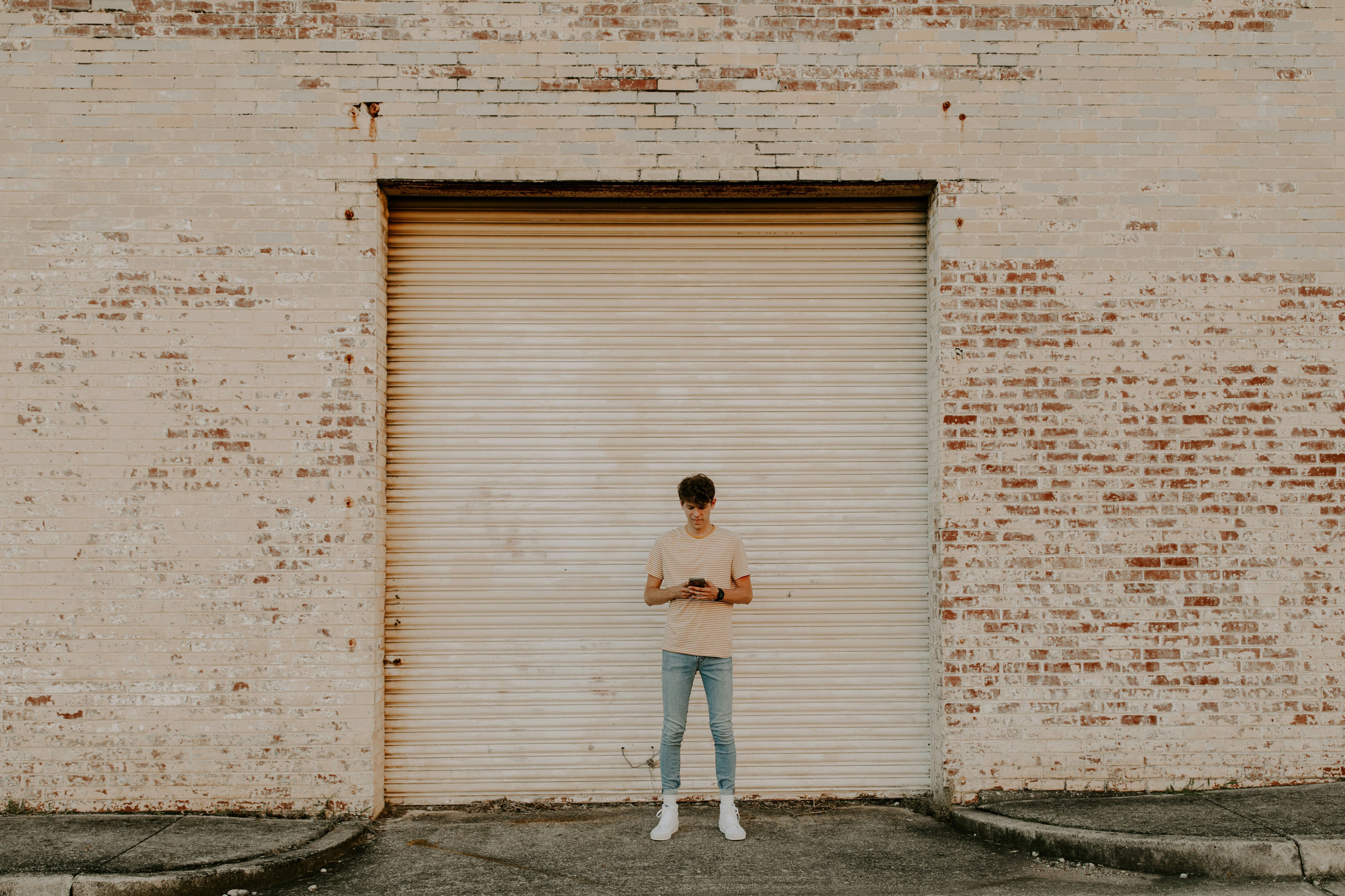 woman in white shirt and blue denim jeans standing beside white wall during daytime