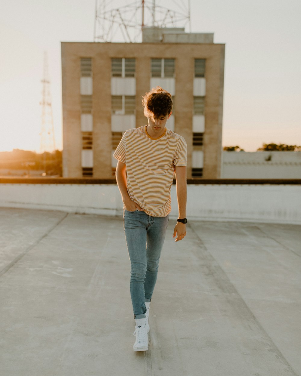 uomo in canotta bianca e jeans blu denim in piedi sul pavimento di cemento grigio durante il giorno