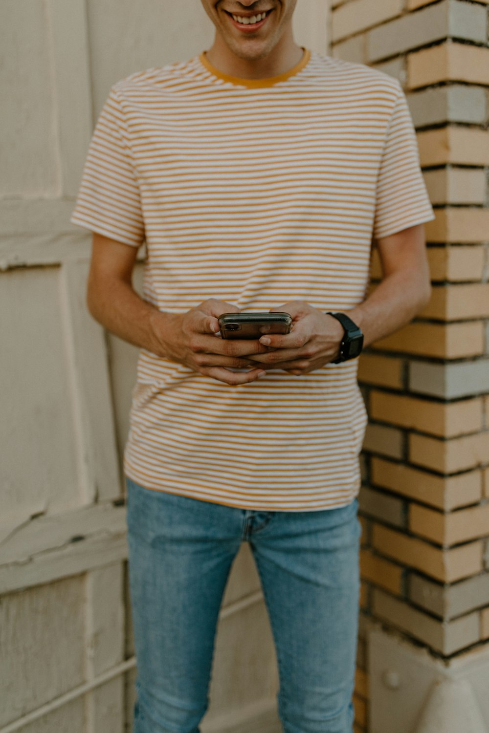 흰색과 검은색 줄무늬 셔츠와 파란색 데님 청바지를 입은 남자가 검은색 스마트폰을 들고 있다