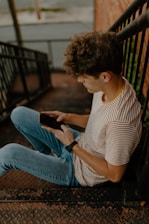 man in white and brown stripe shirt and blue denim jeans sitting on brown wooden bench