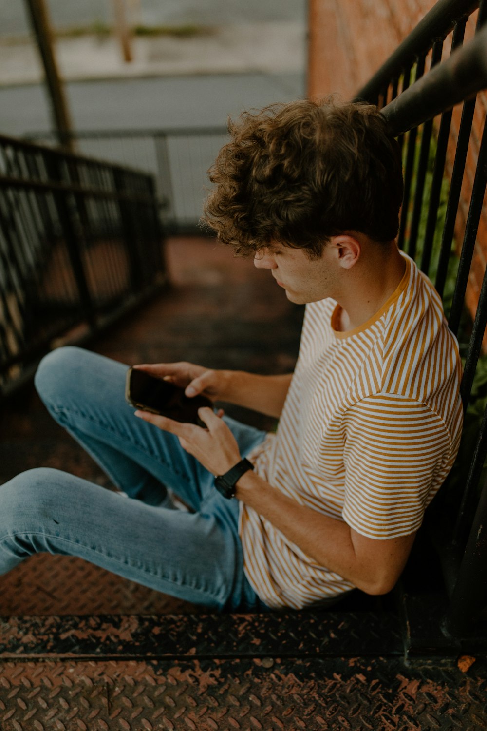 man in white and brown stripe shirt and blue denim jeans sitting on brown wooden bench