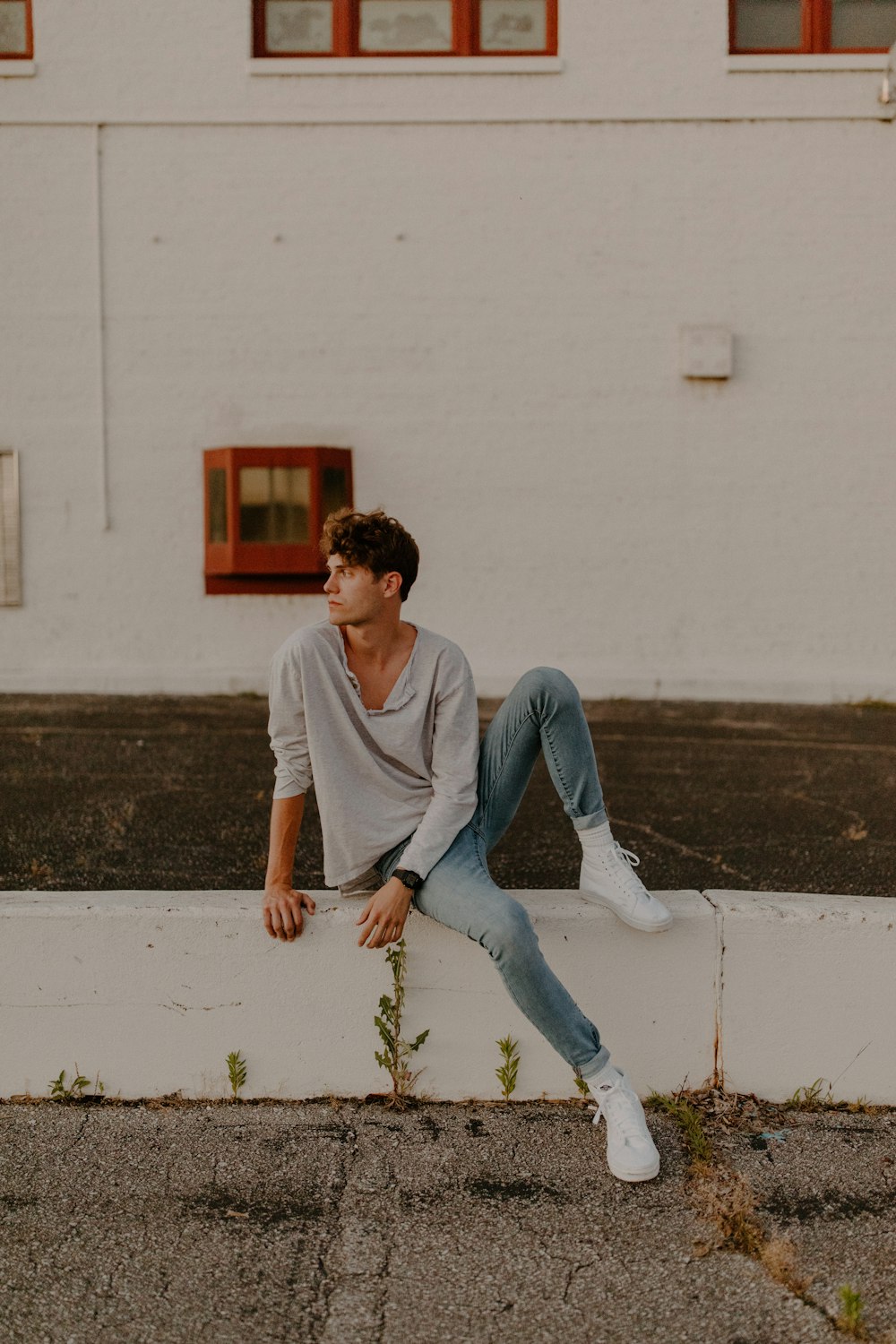 man in white crew neck t-shirt and blue denim jeans sitting on white concrete wall