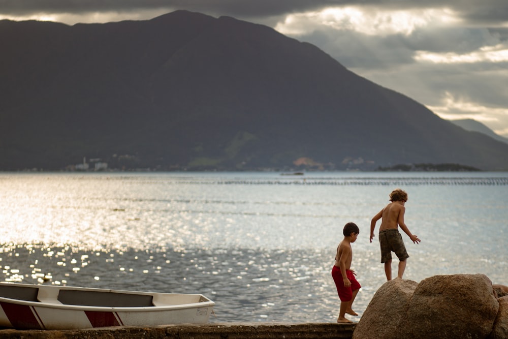 昼間、水辺の岩の上に立つ2人の少年