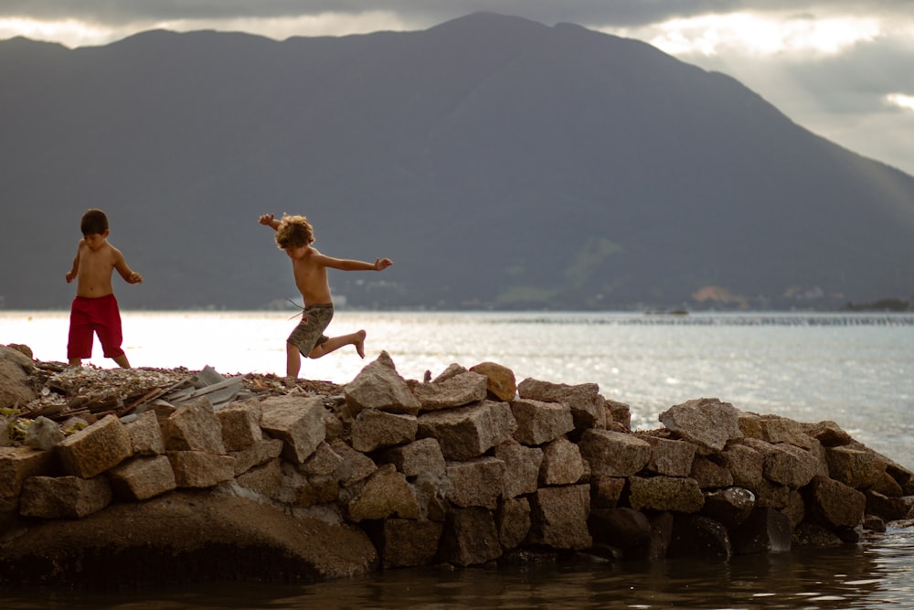 woman in black bikini jumping on rocky shore during daytime