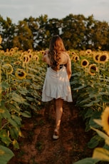 girl in white dress standing on sunflower field during daytime