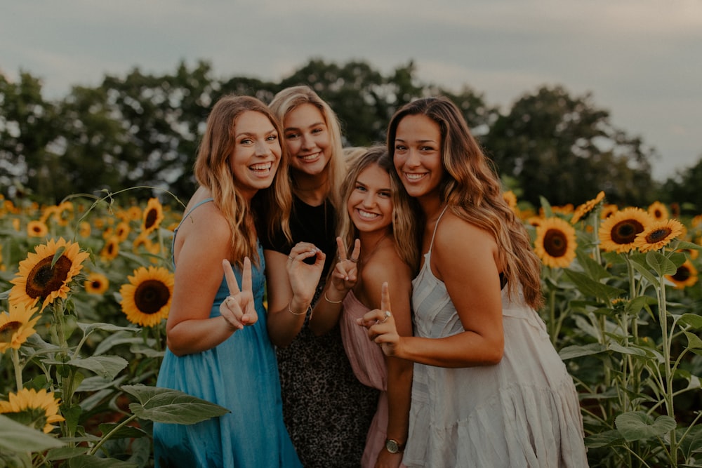 3 women smiling and standing on sunflower field during daytime