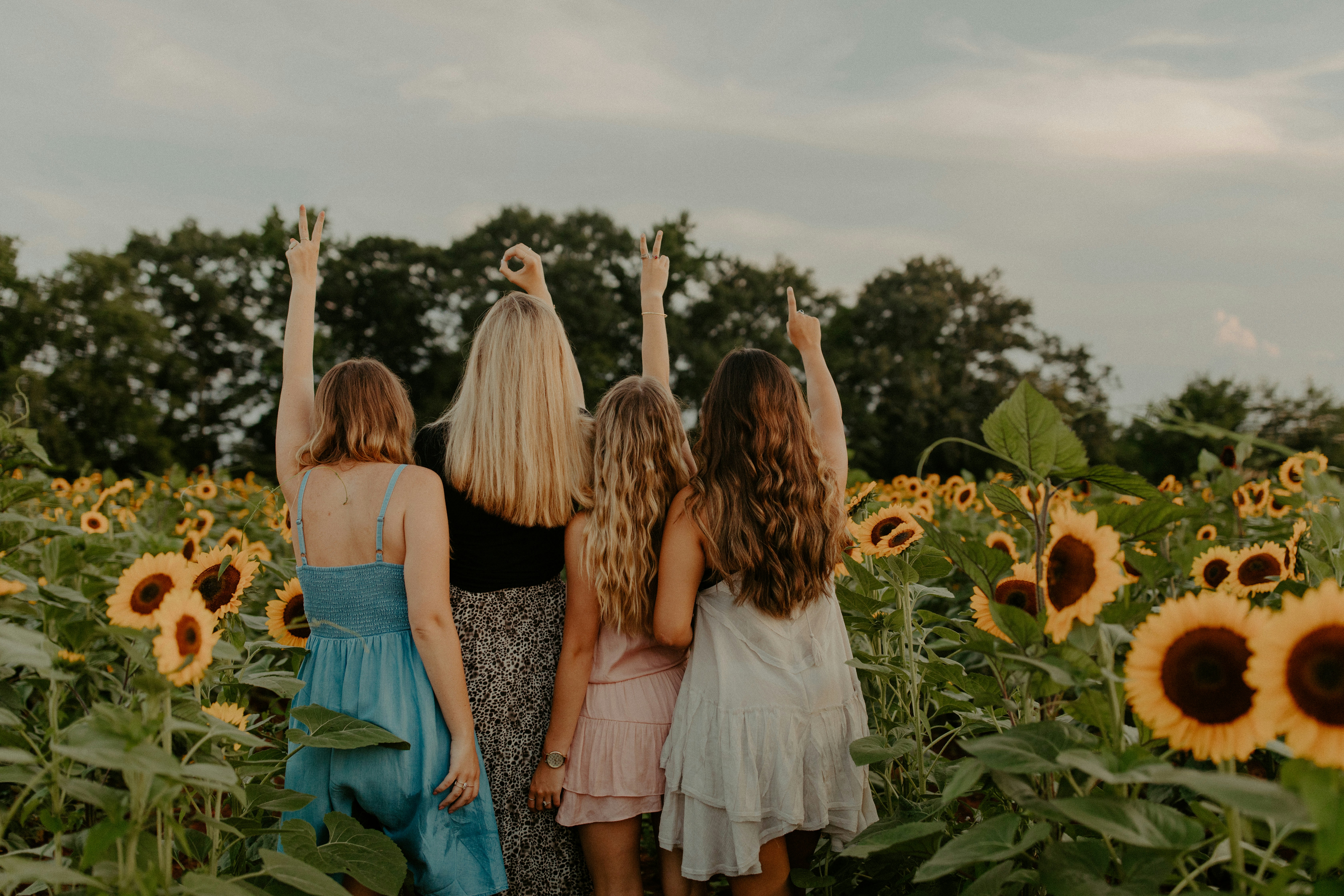 college girls laughing together holding hands in the air in a sunflower field spelling out 2021