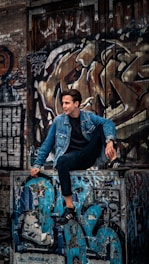 man in blue denim jacket and black pants sitting on black metal fence