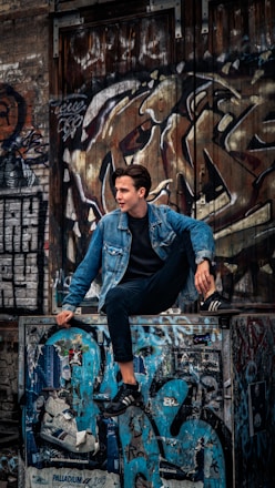 man in blue denim jacket and black pants sitting on black metal fence