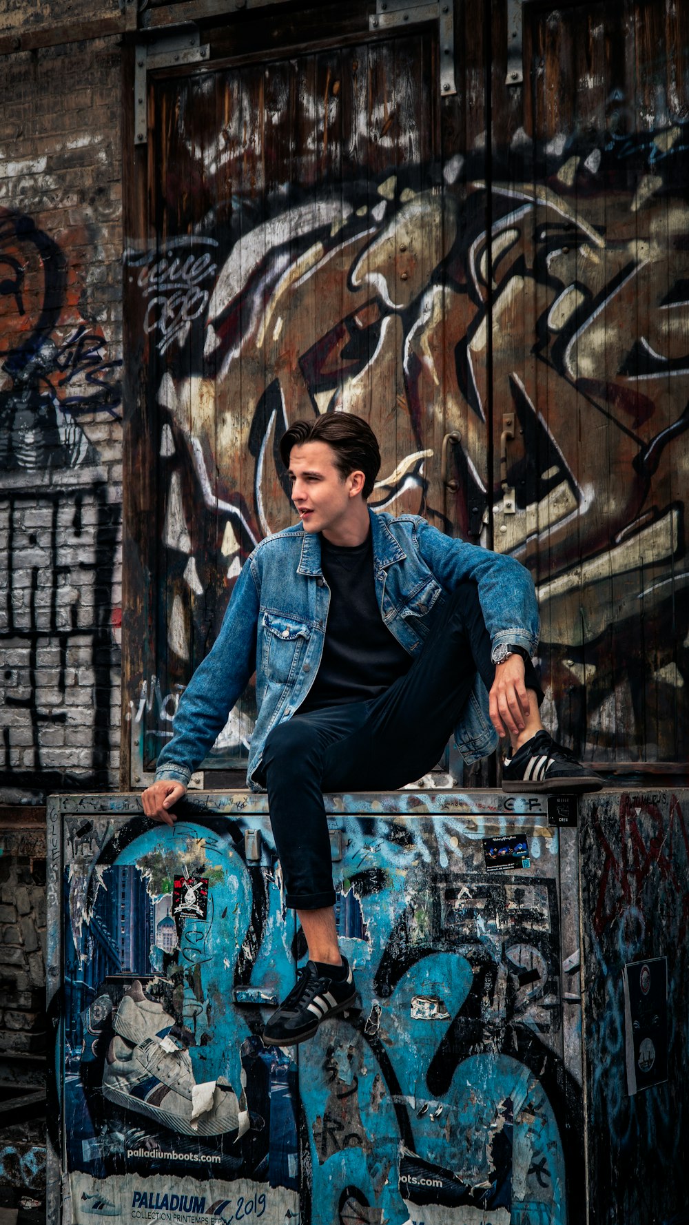 man in blue denim jacket and black pants sitting on black metal fence