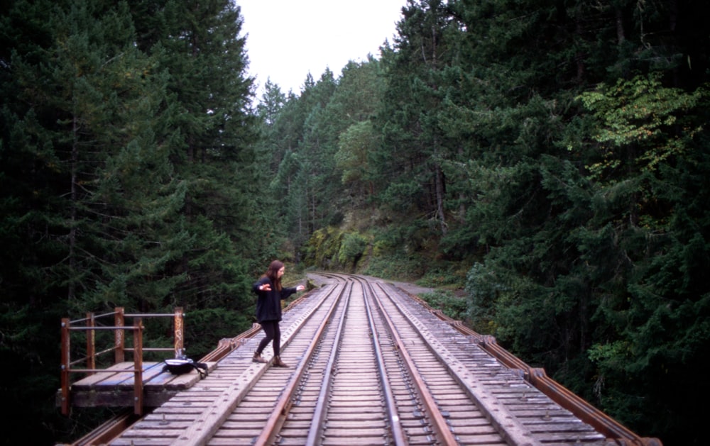 woman in black jacket walking on train rail during daytime