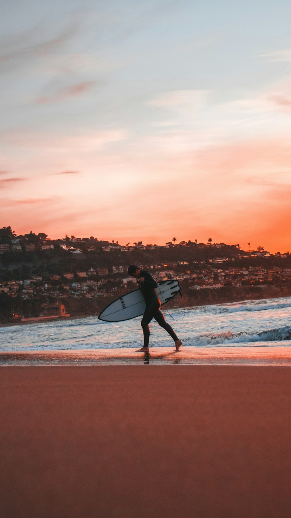 man in black wet suit holding white surfboard walking on beach during sunset