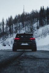 A sleek black luxury vehicle parked beside a snow-covered mountain lodge during golden hour.