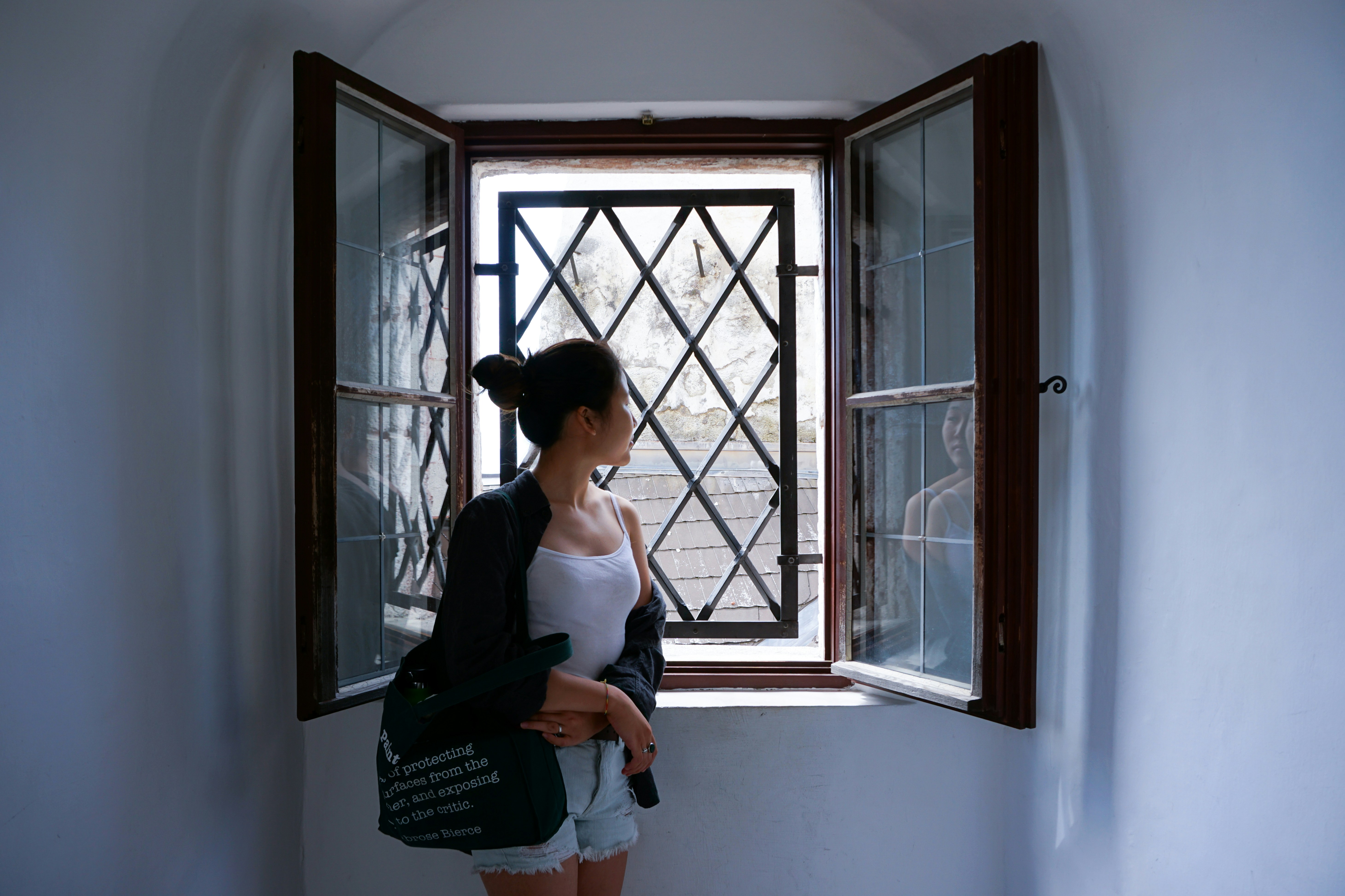woman in black tank top and white pants standing beside window