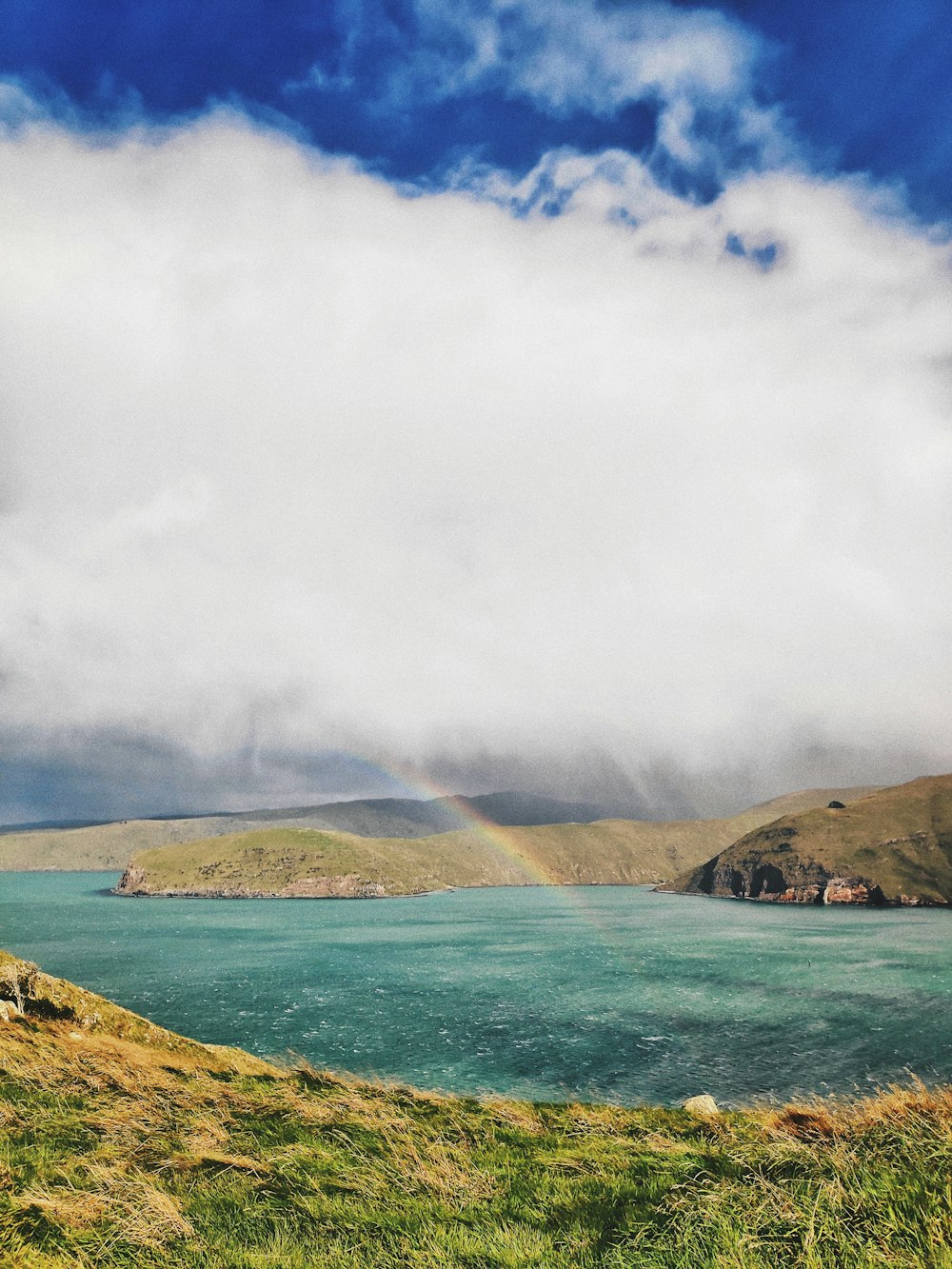 green mountain beside body of water under white clouds during daytime