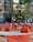 Barriers and orange mesh fencing are set up around a construction area on the street, with a yellow building and surrounding trees in the background. The barriers are placed in an orderly fashion, indicating ongoing roadwork or maintenance.