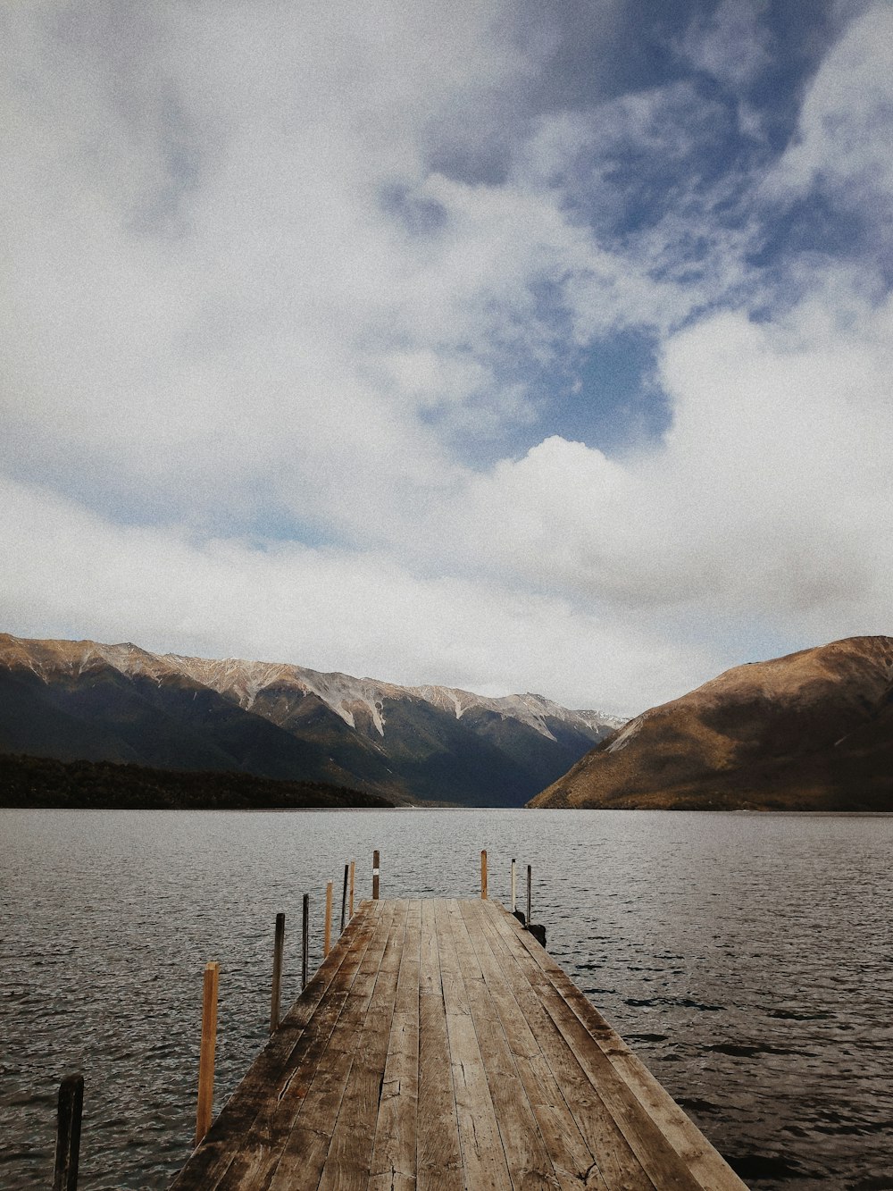 Quai en bois brun sur le lac près de la montagne sous les nuages blancs pendant la journée