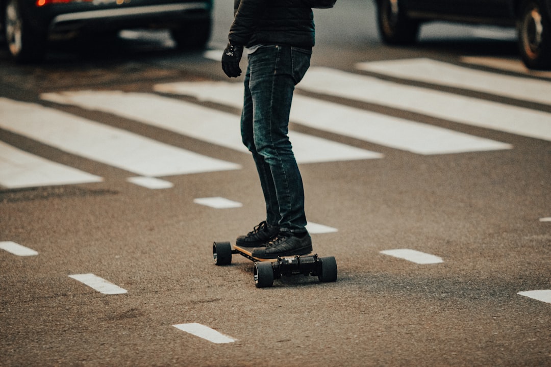 person in black jacket and blue denim jeans walking on pedestrian lane during daytime