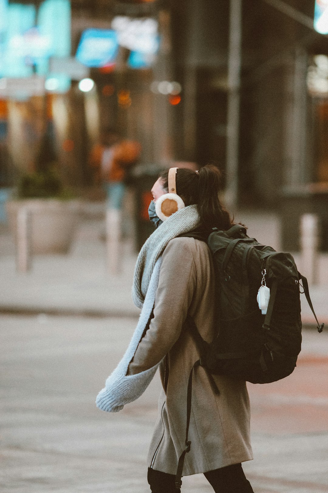 woman in gray coat and white knit scarf with black backpack walking on street during daytime