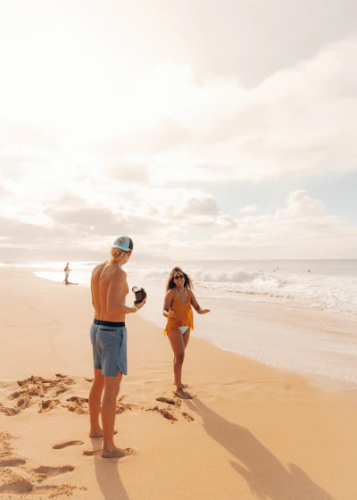 A sun-drenched candid shot of a couple laughing softly while holding hands on a sandy beach