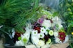 A collection of floral arrangements featuring white, red, and purple flowers mixed with greenery, including long pine needles. The bouquets are wrapped in clear plastic, highlighting the vibrant colors and diverse textures of the blooms.