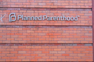 A rectangular brick wall with a sign that has the words 'Planned Parenthood' written in metal letters attached to it.