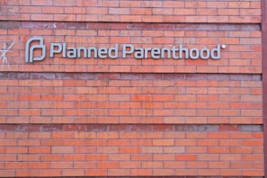A rectangular brick wall with a sign that has the words 'Planned Parenthood' written in metal letters attached to it.