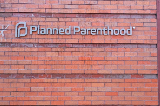 A rectangular brick wall with a sign that has the words 'Planned Parenthood' written in metal letters attached to it.