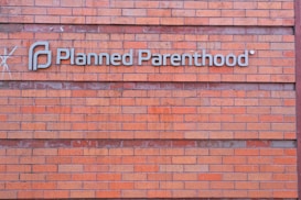 A rectangular brick wall with a sign that has the words 'Planned Parenthood' written in metal letters attached to it.