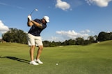 man in black shirt and white shorts playing golf during daytime