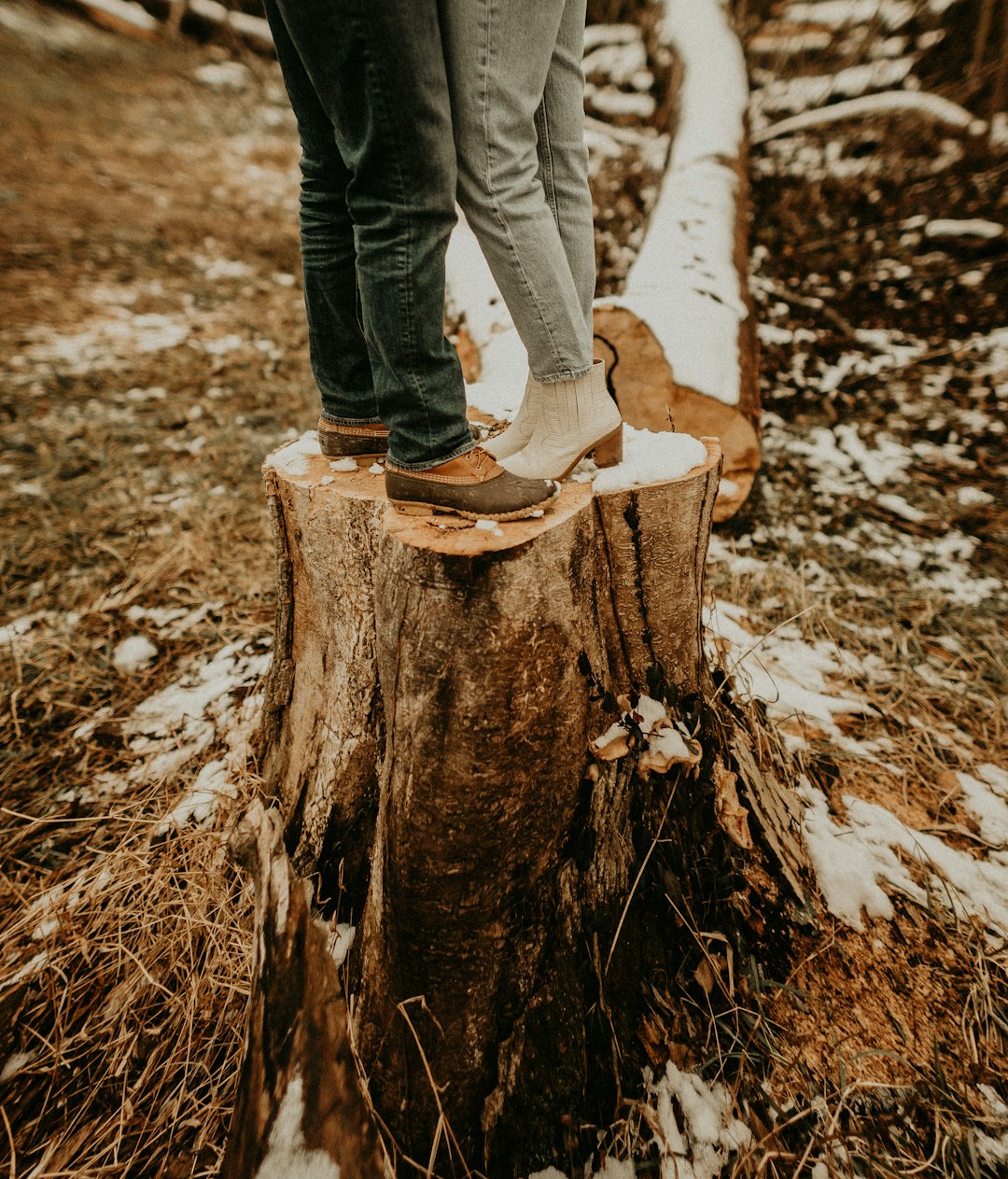 person in blue denim jeans and brown boots standing on brown tree log