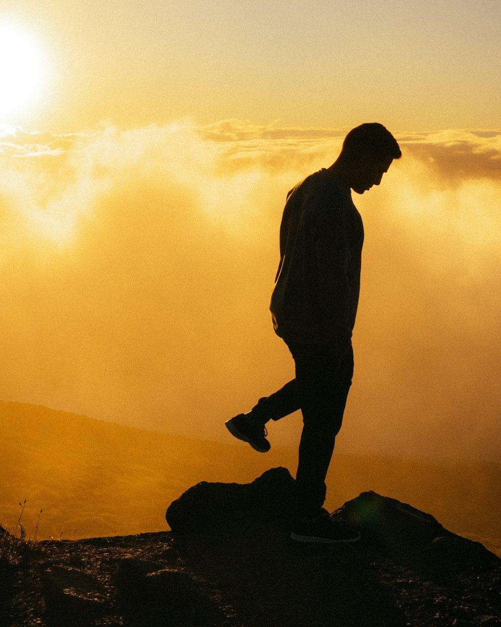 silhouette of man standing on rock during sunset