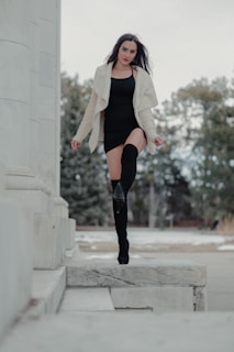 A model walking confidently in sleek black ankle boots and a flowing dress, embodying effortless fashion.