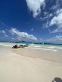 A vibrant boat sailing on turquoise Caribbean waters near a white sandy beach at sunset.