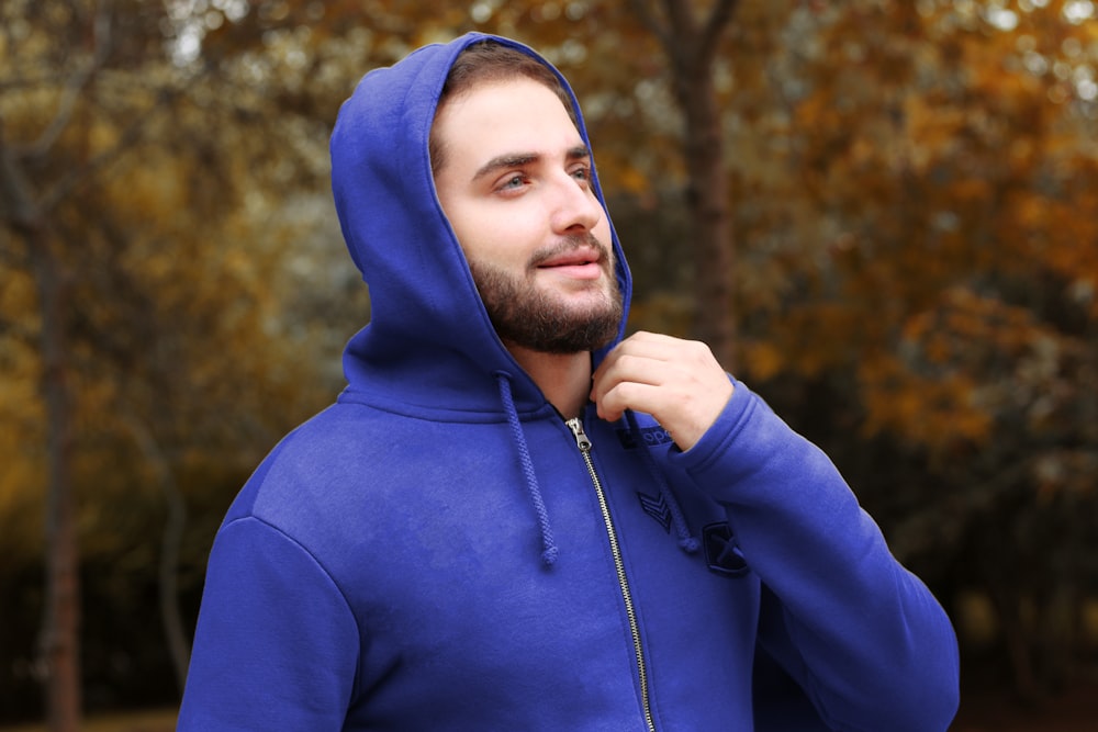 man in blue hoodie standing near trees during daytime