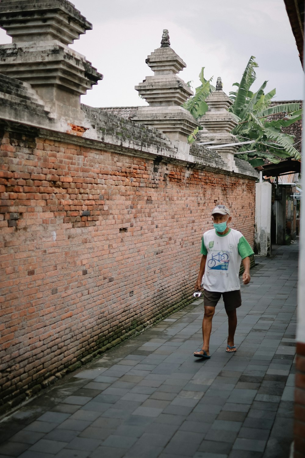 man in white crew neck t-shirt walking on brown brick wall during daytime