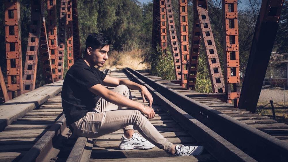 man in black hoodie and gray pants sitting on brown wooden bench