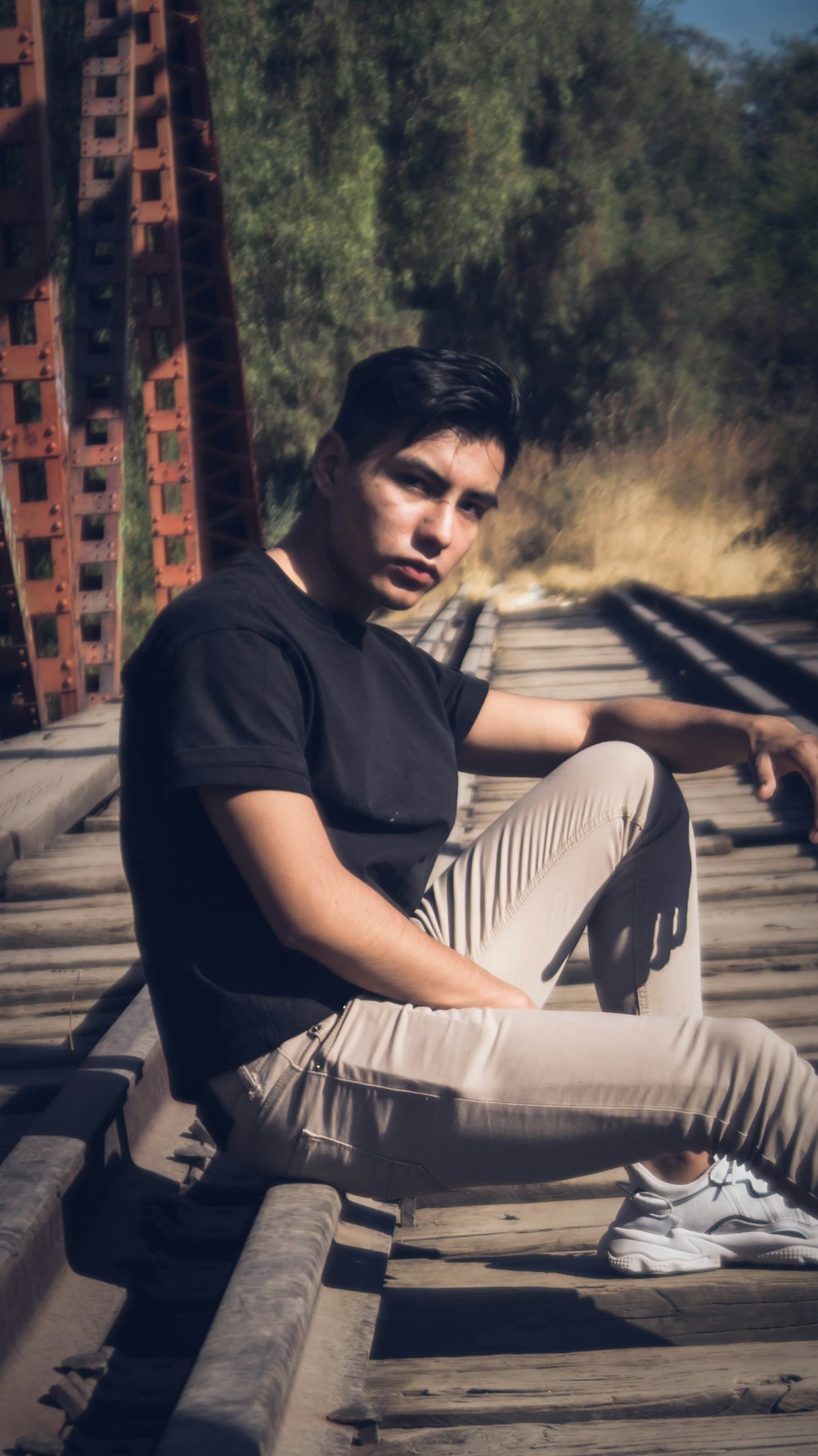 man in black crew neck t-shirt and white pants sitting on brown wooden bench