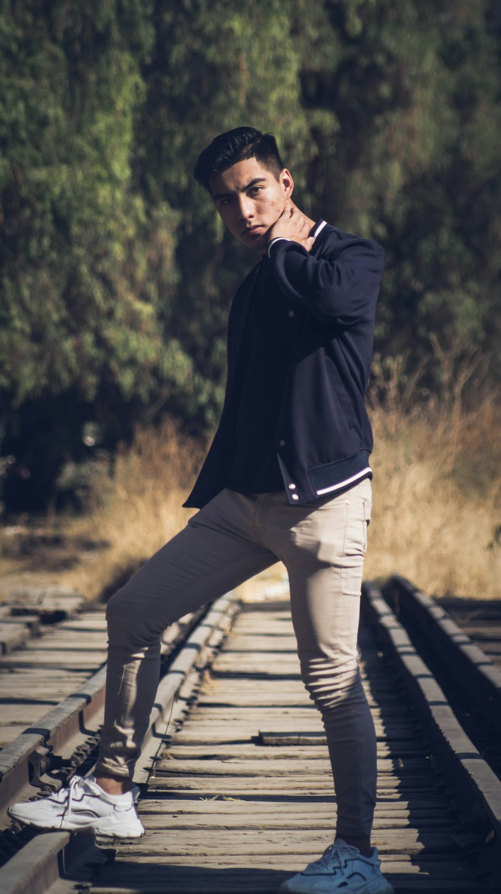 man in black jacket and white pants standing on wooden pathway during daytime