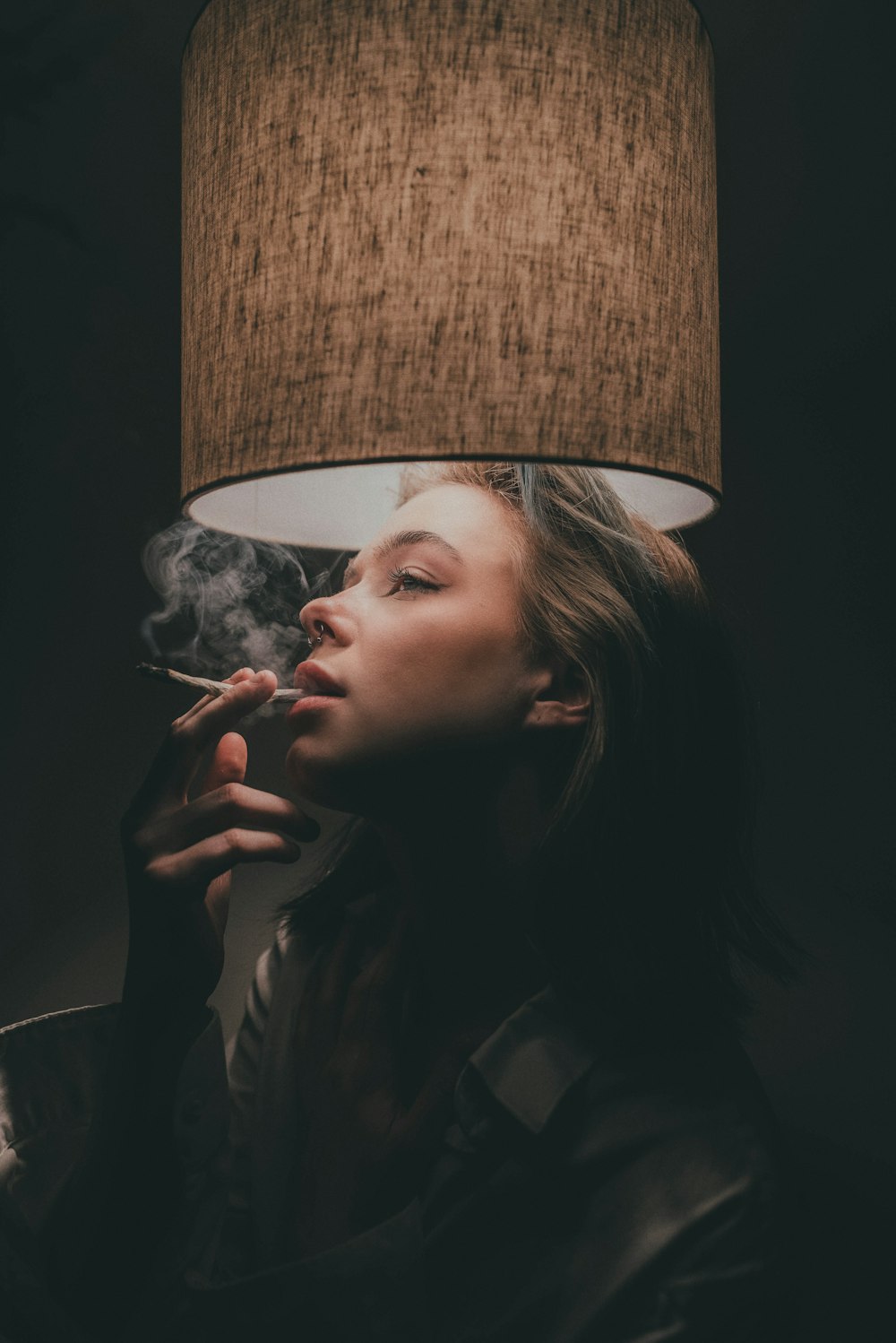 a woman smoking a cigarette next to a lamp
