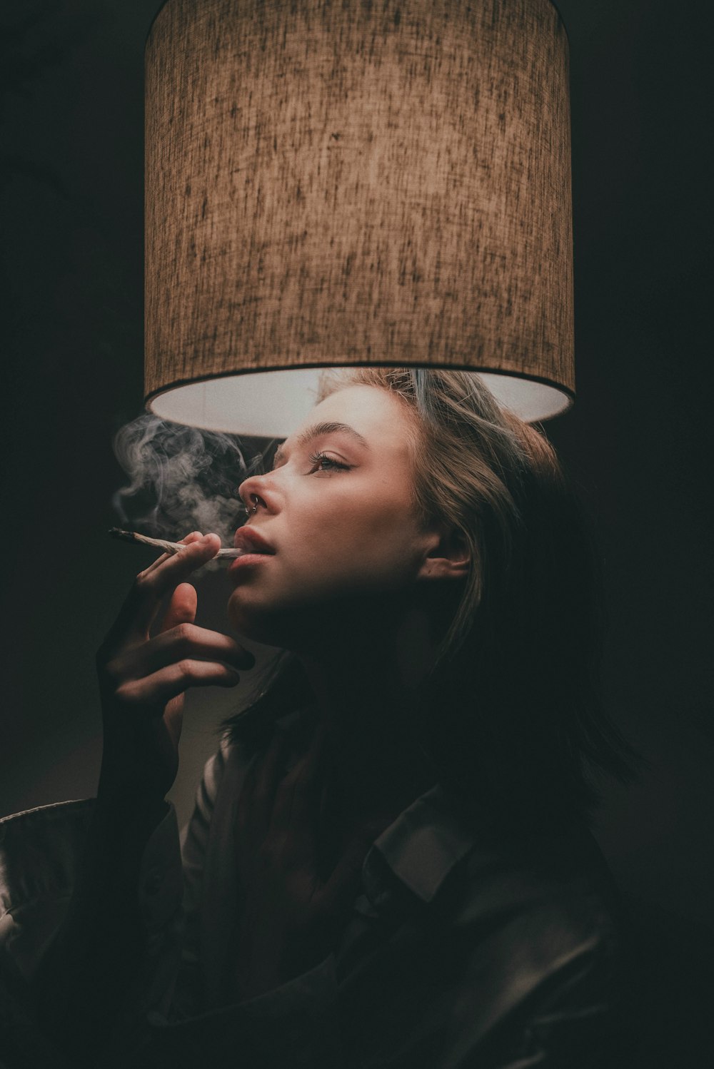 a woman smoking a cigarette next to a lamp