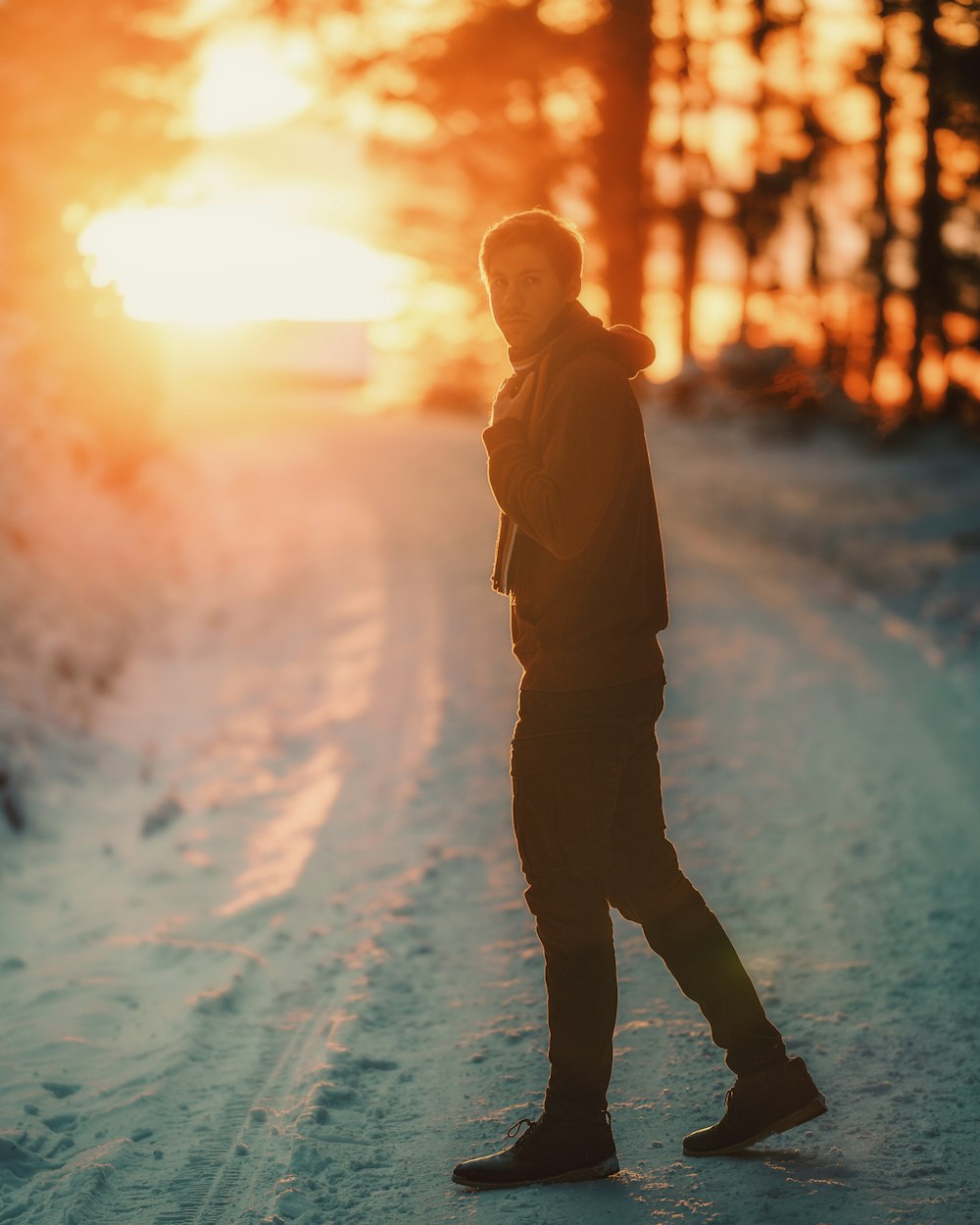 昼間、雪に覆われた地面に立つ茶色のジャケットを着た男性