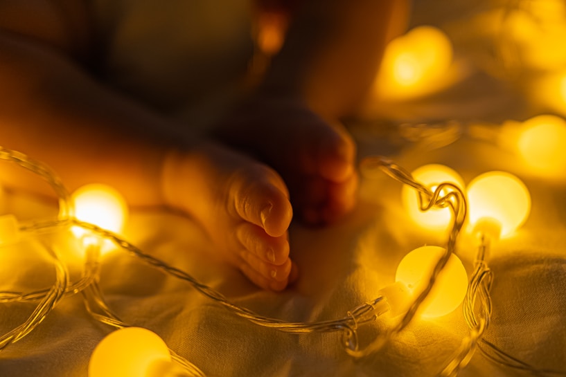 Soft, warm lighting illuminates small infant feet surrounded by glowing string lights, creating a cozy and intimate atmosphere.