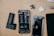 Various components of a disassembled smartphone are spread out on a wooden surface. Visible parts include the phone battery, camera module, front screen panel, and several small repair tools. The disassembled phone reveals intricate internal electronics.