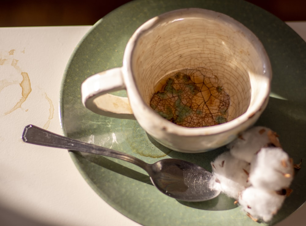 white ceramic mug beside stainless steel spoon