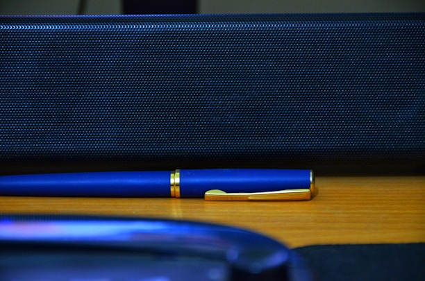 A sleek gold pen on a minimalist white marble desk beside a voice command device.