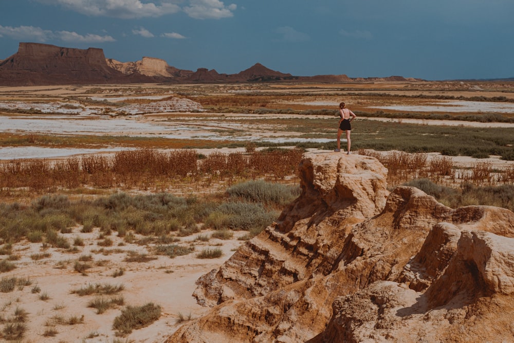 woman in white shirt and black pants standing on brown rock formation during daytime