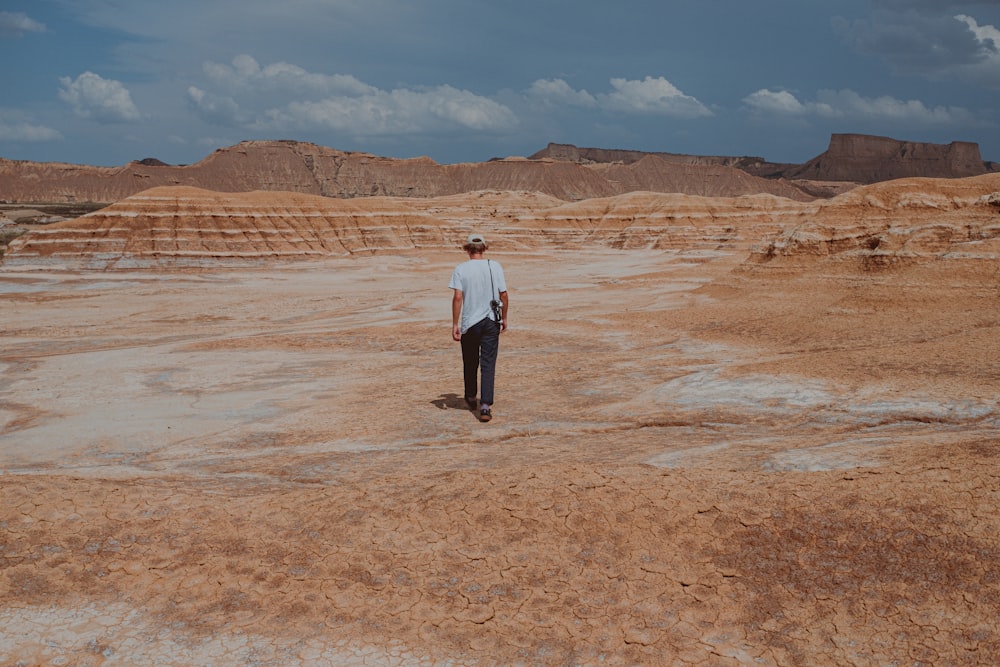 man in white dress shirt and black pants standing on brown sand during daytime