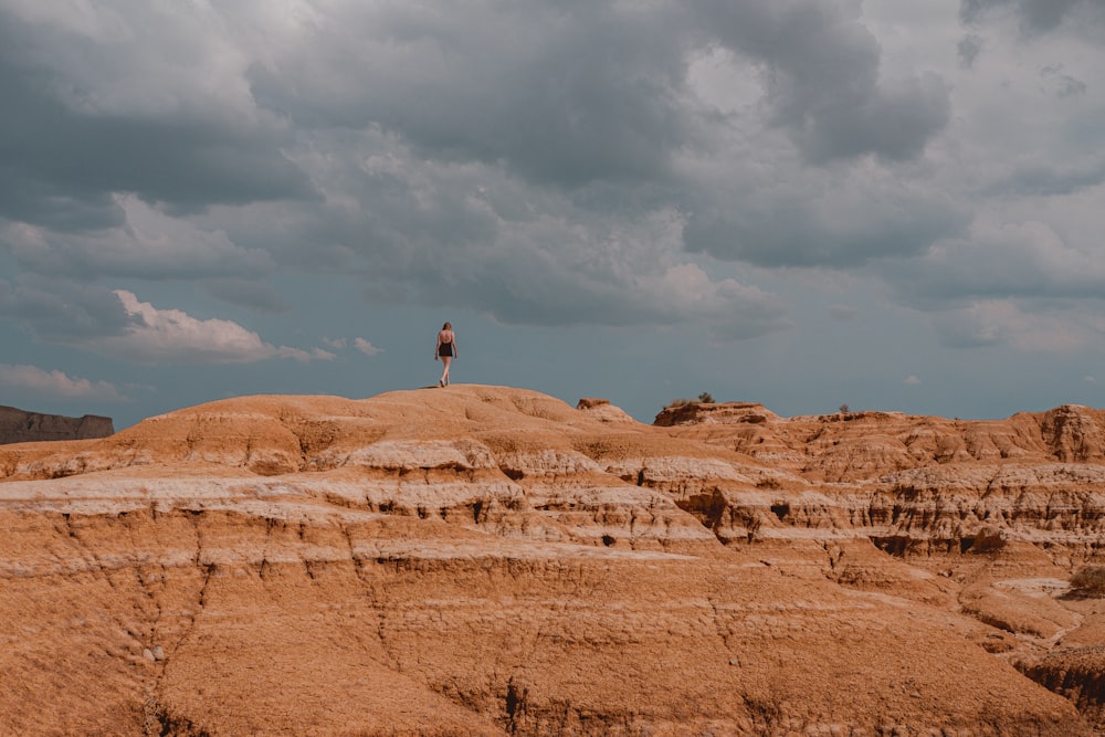 person in black jacket and white pants walking on brown field under white clouds and blue