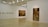 A minimalistic art gallery with white walls displays several pieces of modern art. Smaller framed artworks are aligned on the left wall, while two large paintings are prominently showcased on the right and central walls. The flooring is neutral-toned, and the ceiling features geometric light fixtures providing even illumination.